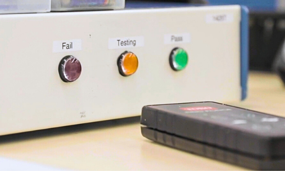 A close up of the front panel of our functional tester, showing Fail, Testing, and Pass along with a remote to control the tester.