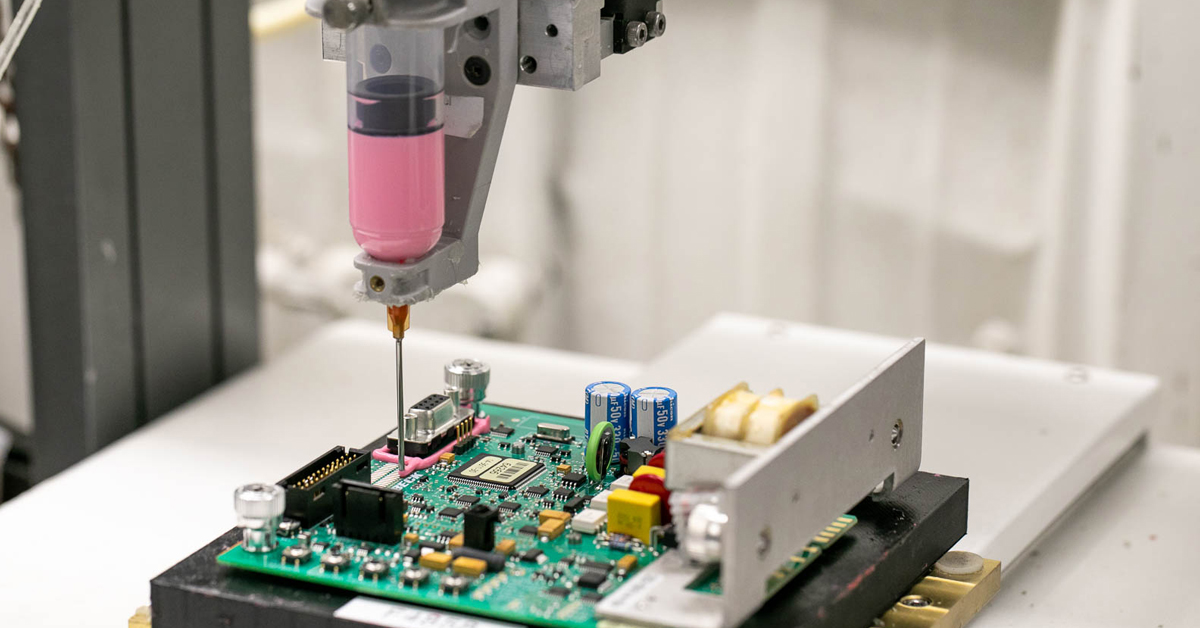 Close up of  a cobot adding protective material to a PCBA.